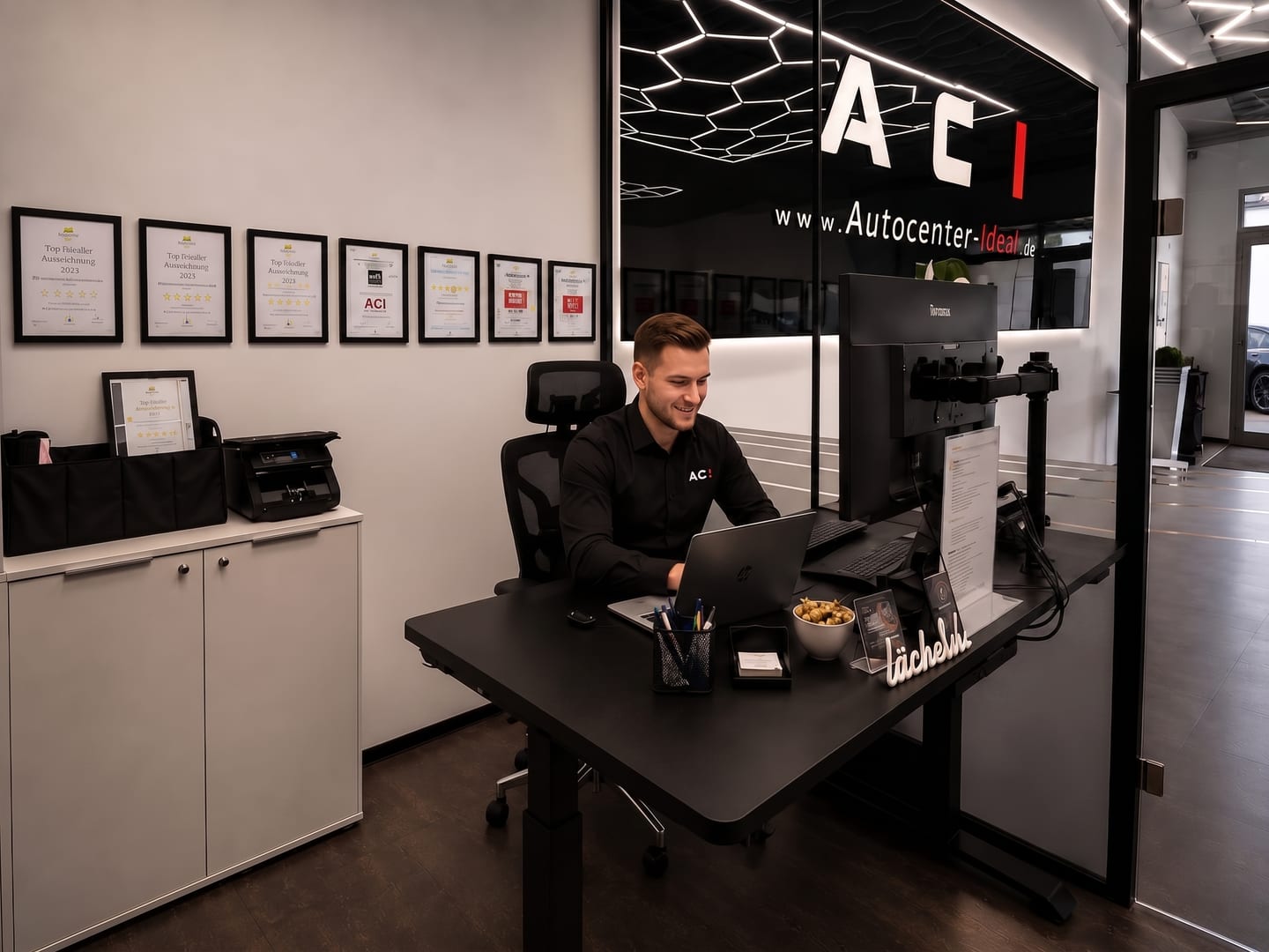 Arbeitsplatz im Büro von Autocenter IDEAL vor der Wand mit Händler-Auszeichnungen